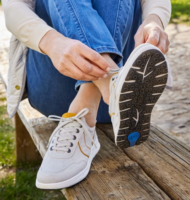 Dame sitzt auf einer Bank und schnürt sich Ihre hellen Sneaker.