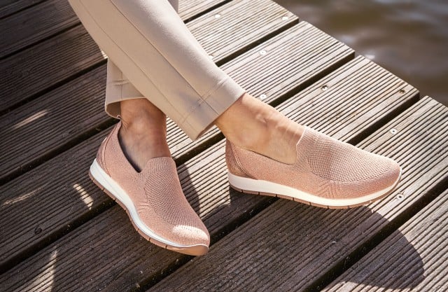 Damenbeine mit beigefarbener Hose tragen rosafarbene Slipper.