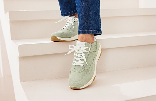 Damenbeine mit blauer Jeans tragen ein mintfarbenes Sneakerpaar.