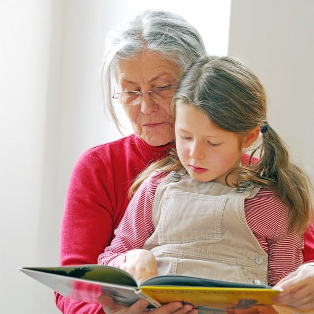 Mädchen sitzt auf Omas Schoß und schaut sich ein Buch an. Mädchen sitzt auf Omas Schoß und schaut sich ein Buch an.