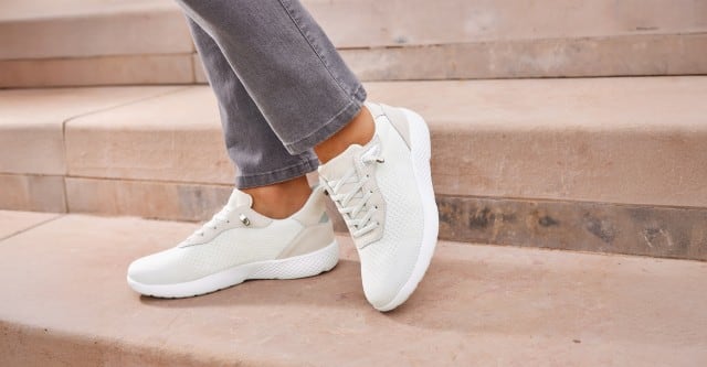 Weiße Sneaker trägt eine Dame mit grauer Jeanshose und geht Steintreppen hinunter.