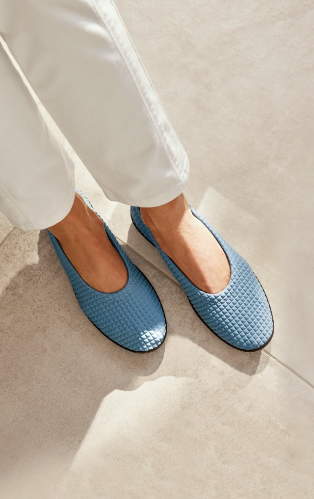 Damenbeine in weißer Hose tragen hellblaue Hallux-Slipper.