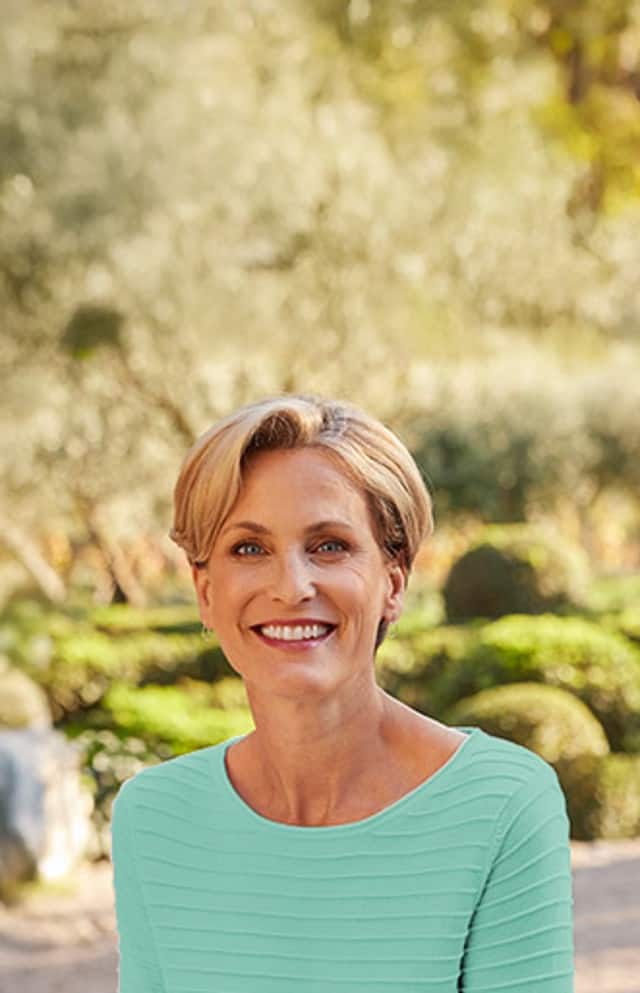 Frau steht in einem Frühlingspark und trägt türkisfarbenen Struktur-Ringel Pullover.