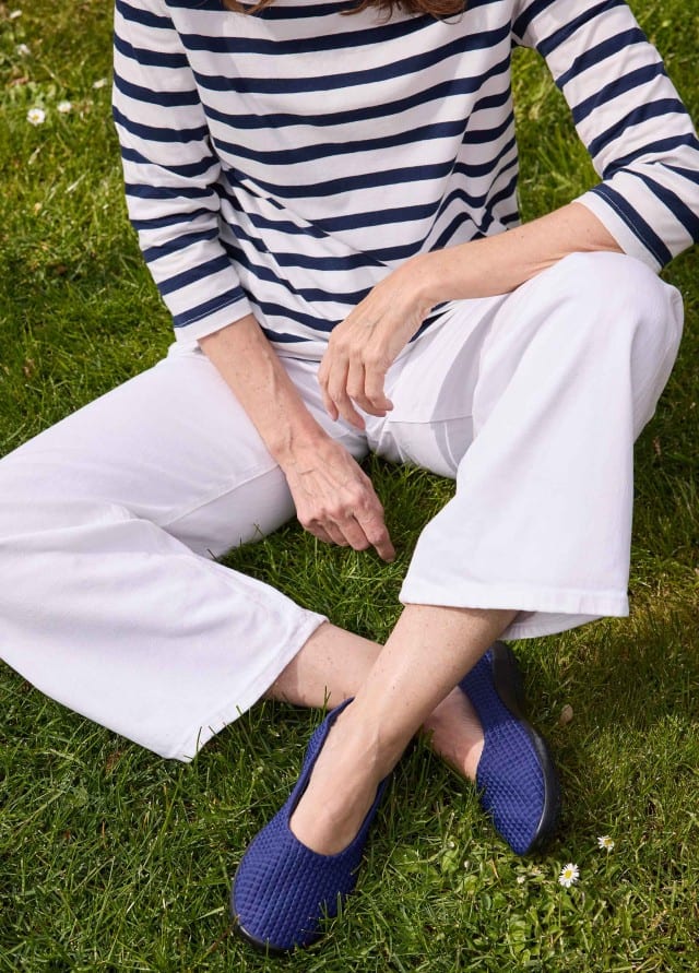 Frau sitzt auf einer Sommerwiese und trägt die Hallux-Softslipper in der Farbe Blau.