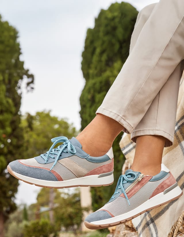 Dame sitzt auf einer Mauer und trägt Hallux-Sneaker Multicolor.