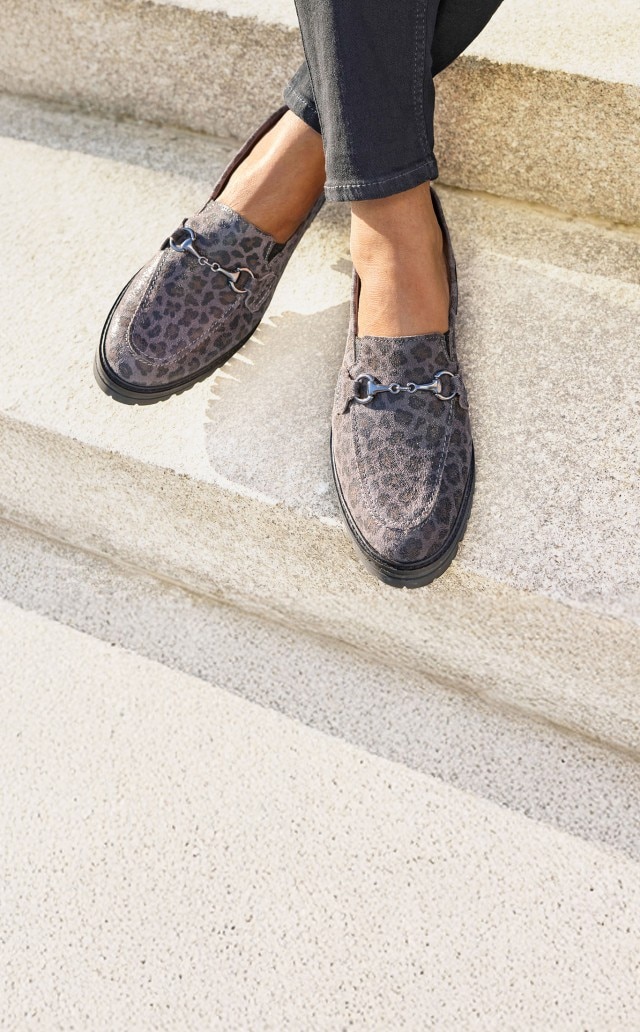 Dame sitzt auf heller Steintreppe und trägt die modischen und bequemen Hallux-Slipper-Schrittsicher im Leoprint.