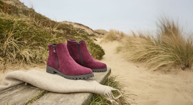 Die Hallux-Stiefelette Kuschelweich steht in der Trendfarbe Bordeaux am Strand.