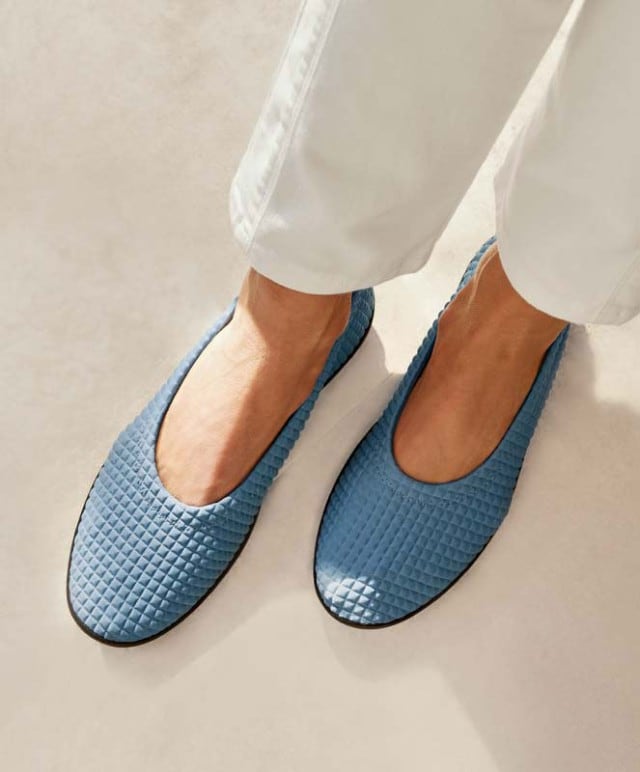 Fröhliche Dame hält ein Paar fliederfarbene Hallux-Schuhe in den Händen.