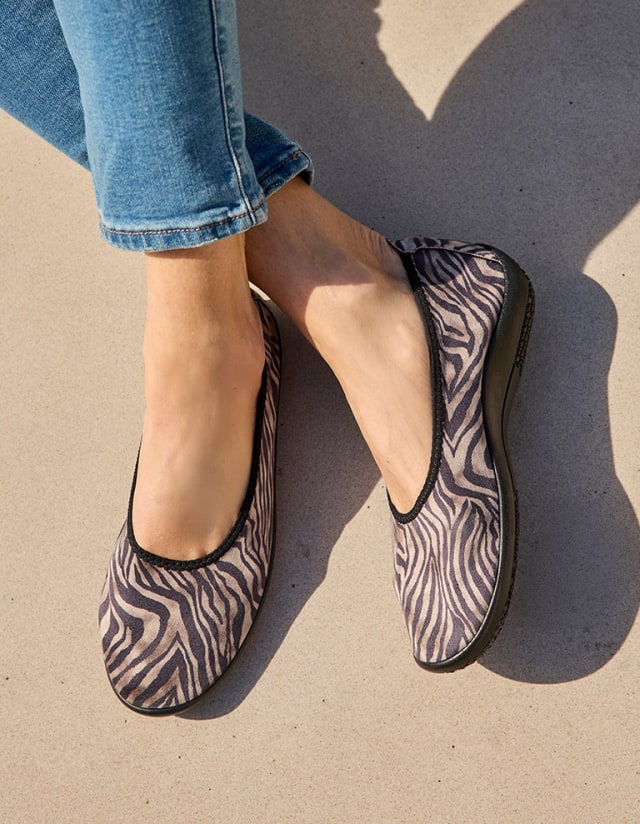 Dame sitzt auf einem hellen Boden und trägt die Hallux-Softslipper Animalprint mit dem Muster Zebra.
