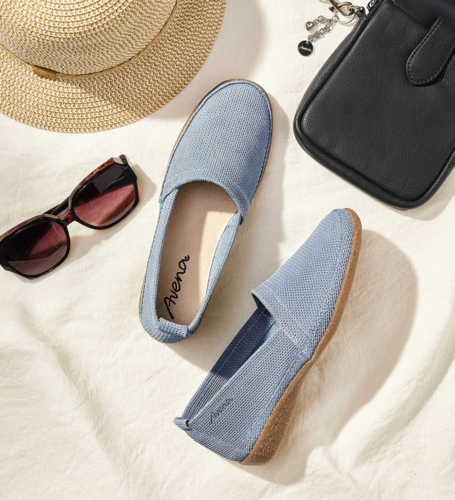 Derm Butterweich-Slipper liegt in einer Urlaubsszenerie mit Tasche, Strohhut und Sonnenbrille.