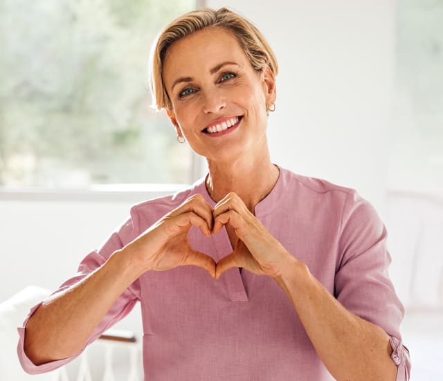 Strahlende Dame zeigt ein aus Händen geformtes Herz.