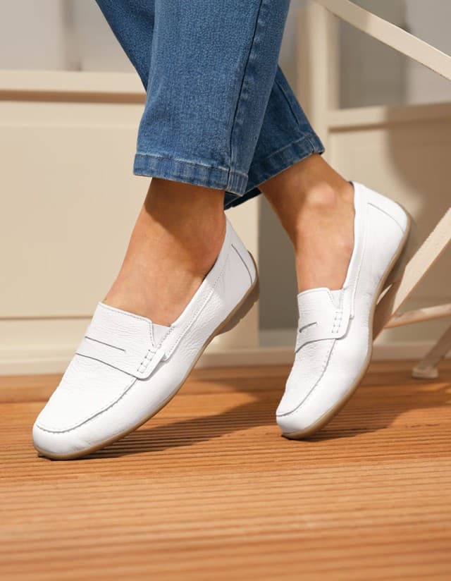 Die Hirschleder-Slipper-Supersoft in Weiß auf einer Holz-Terrasse werden getragen.