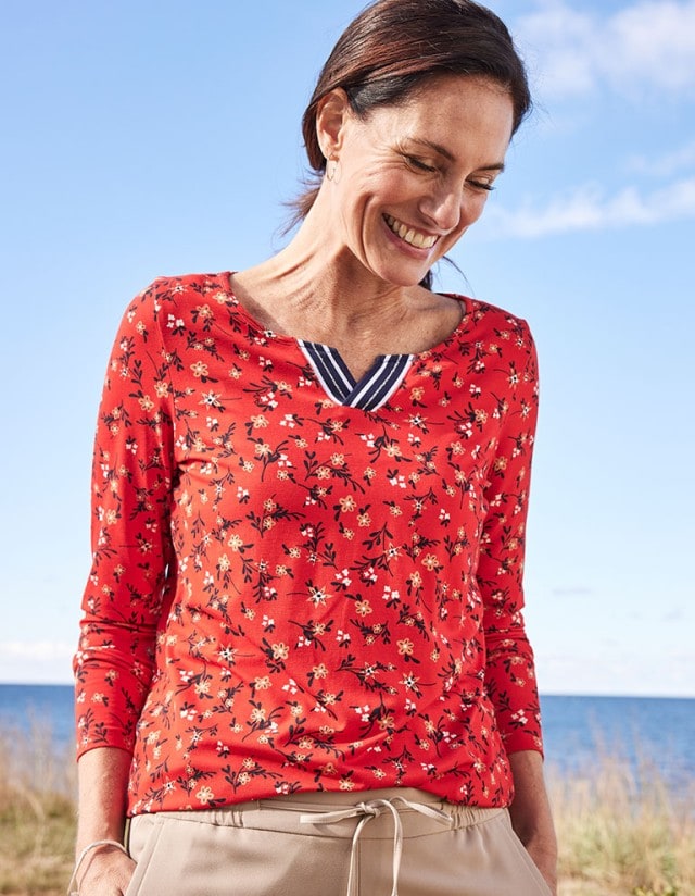 Dame am Strand trägt rot-geblümtes Langarmshirt.