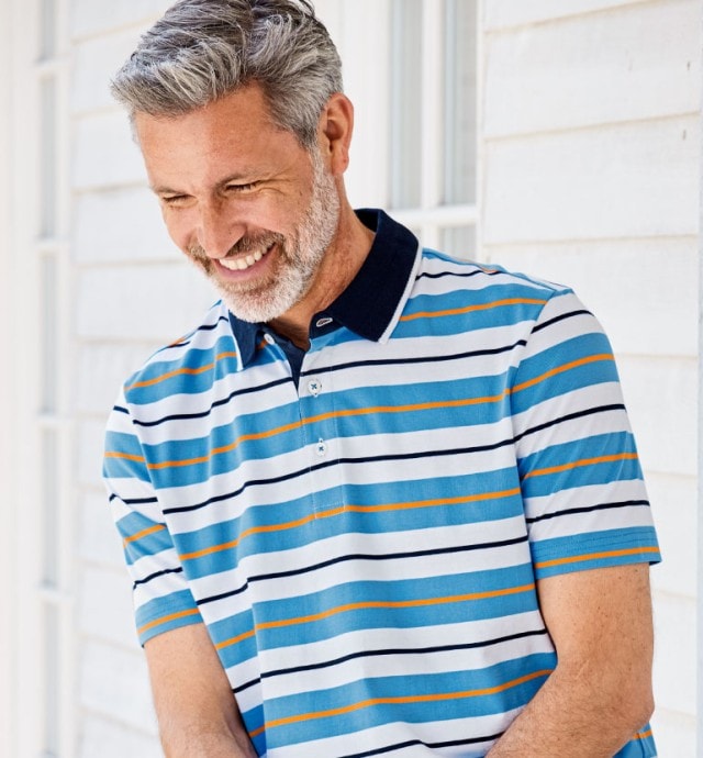 Lächelnder Herr steht auf einer freundlichen Veranda und trägt Kurzarm-Poloshirt Streifen in dem Dessin Blau gestreift. 
Das Shirt ist im SALE.
