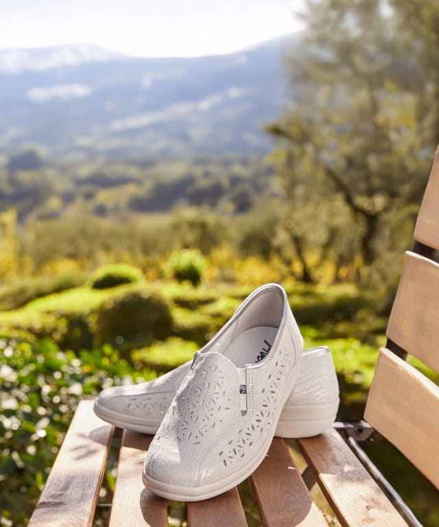 Die wunderbar leichten Luftpolster-Bequemslipper werden auf einem Holzstuhl mit Blick ins Grüne präsentiert.