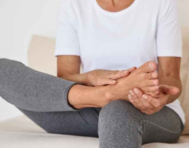 Eine sitzende Frau hält Ihren Fuß in den Händen