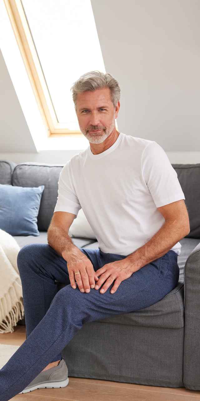 Ein lächelnder Mann trägt ein weißes TShirt und eine blaue Freizeithose.