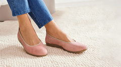 Frau in blauen Jeans trägt rosa Ballerinas auf einem hellen Teppich.