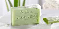 Grüne Seife mit Aloe Vera, Schaum an der Ecke, auf einem Tisch neben einem geschnittenen Aloe-Blatt, mit verschwommenem Hintergrund.
