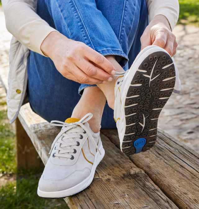 Dame sitzt auf einer Bank und schnürt sich Ihre hellen Sneaker.