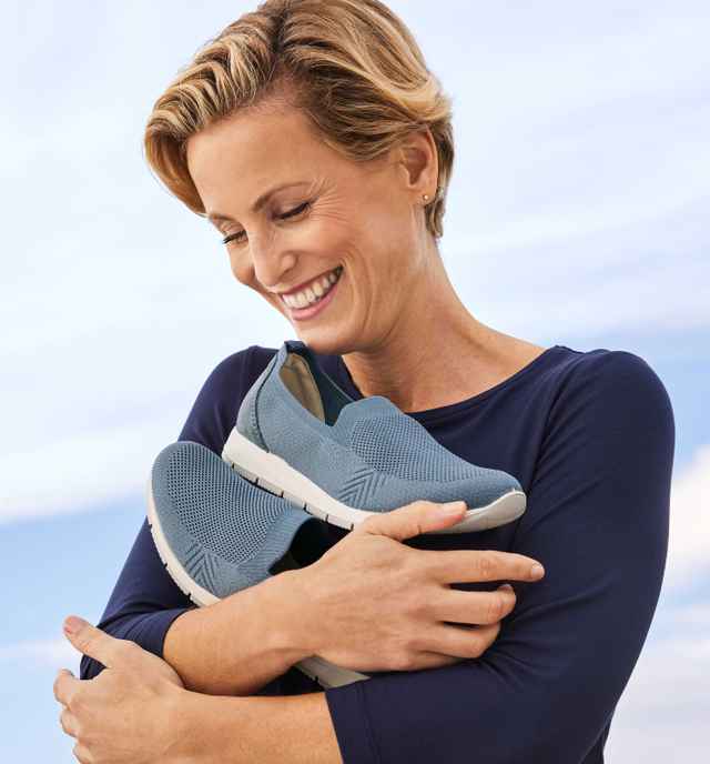 Auf dem Arm hält eine Frau ein Paar Slipper in Hellblau