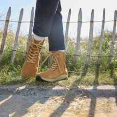 Person in Jeans und Stiefeln steht vor einem Holzzaun auf einer Wiese. Sonne scheint.