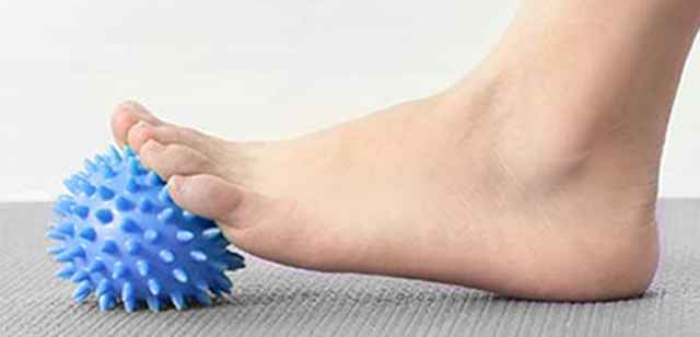 Fuß rollt über blauen stacheligen Ball auf grauer Unterlage, zur Massage oder Entspannung der Fußsohle.