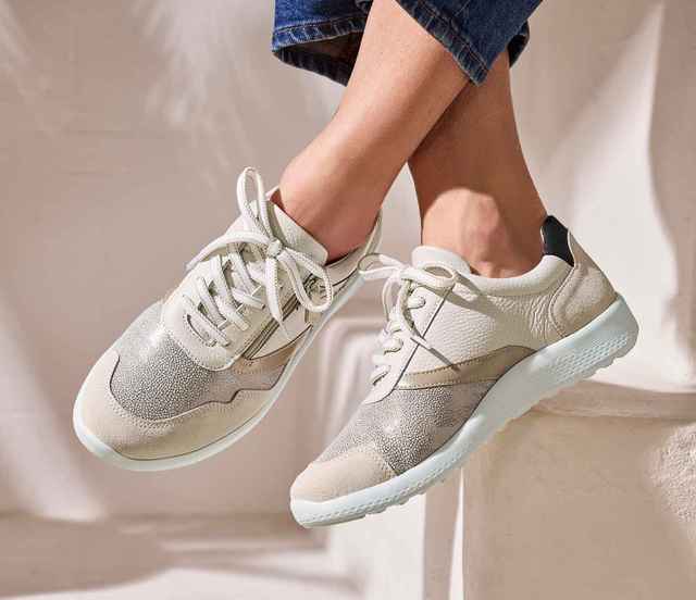 Dame sitzt auf einer hellen Treppe und trägt die Hallux-Schnürer-Extraweit in Beige.