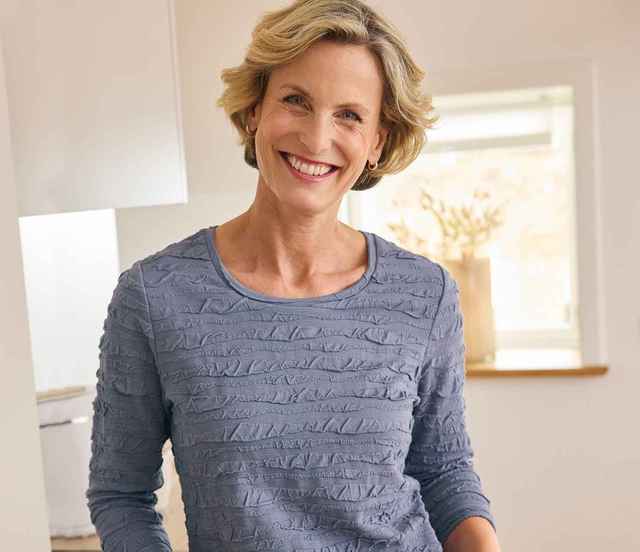 Dame in hellem Wohnraum trägt das granitblaue Rundhals-Shirt Strukturmuster.