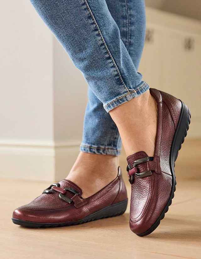 Braune Lederschuhe mit Schnalle, getragen zu hellblauen Jeans auf einem Holzfußboden.