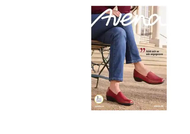 Eine Frau sitzt auf einem Stuhl, sie trägt Jeans und den roten Hirschleder-Slipper.