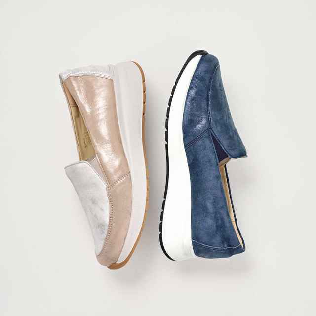 Ein cremefarbener und ein blauer Slip-on-Schuh liegen nebeneinander auf weißem Hintergrund, beide mit dicker weißer Sohle.