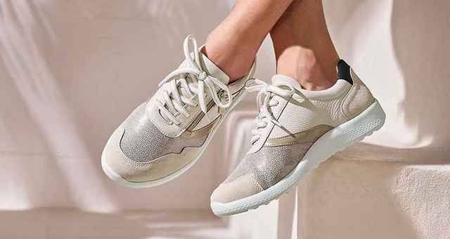 Dame sitzt auf einer hellen Treppe und trägt die Hallux-Schnürer-Extraweit in Beige.