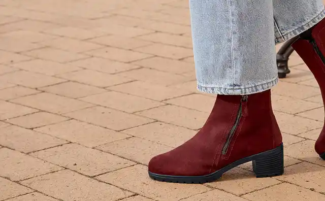 Person in hellroten Stiefeln und Jeans steht auf einem Pflastersteinboden.