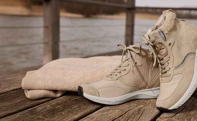 Beige Stiefel und ein Pullover liegen auf einem Holzsteg neben einem Fluss.